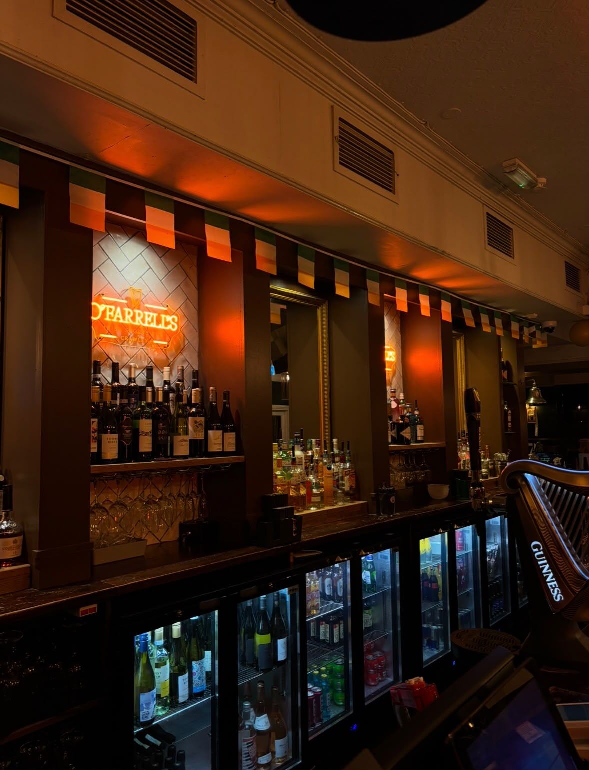 The back bar at O'Farrell's with Irish tricolour bunting along the counter front and shelves of spirits behind