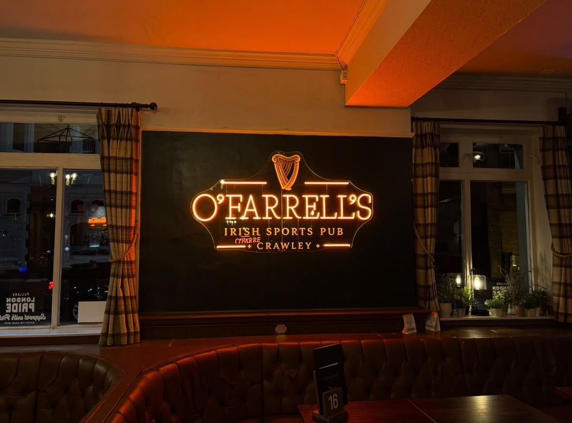 The amber neon O'Farrell's Irish Sports Pub sign glowing on a dark panelled wall inside the pub